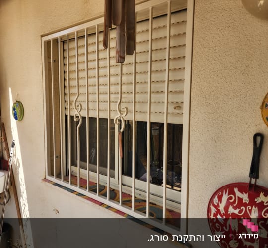 חלון עם סורגים לבנים ותריסים סגורים